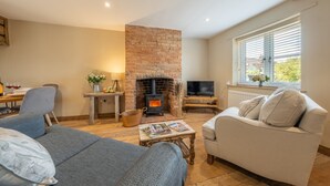 A cozy living room with a fireplace, a sofa, a television, and a dining area with a table and chairs. - Willow Cottage (SC), South Creake, Norfolk (South Creake)