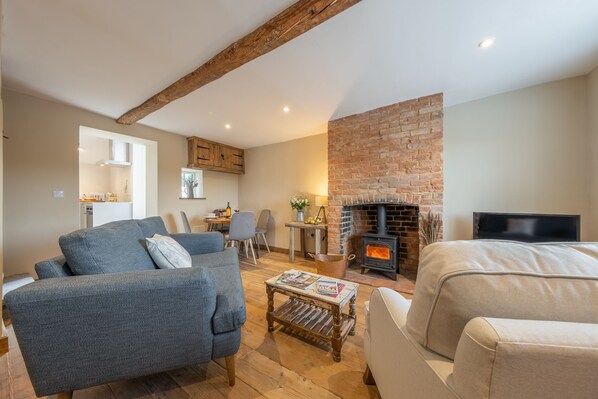 A cozy living room with a fireplace, a sofa, a coffee table, and a TV. - Willow Cottage (SC), South Creake, Norfolk (South Creake)