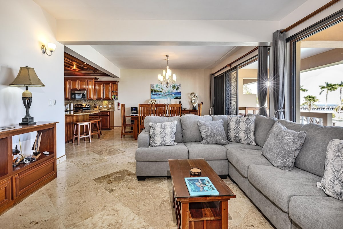 A modern living room with a grey sofa, wooden coffee table, and a dining area with a kitchen in the background.