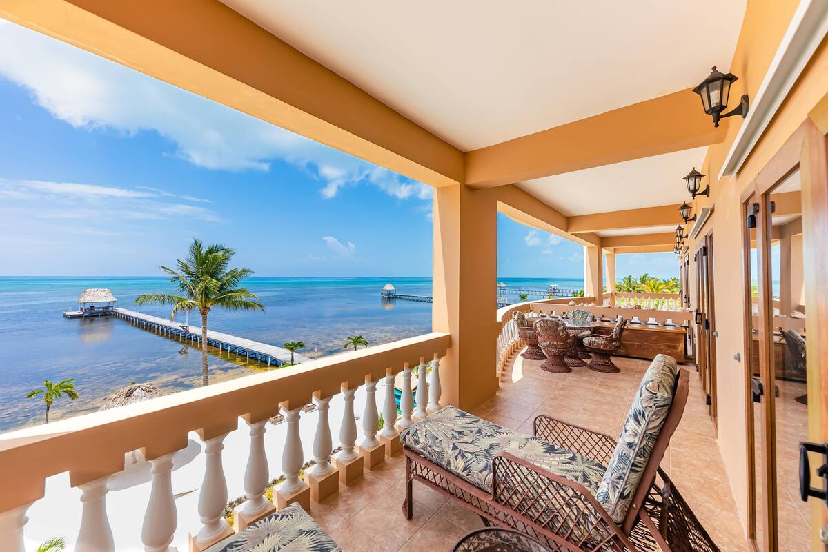 A balcony with wicker furniture, a view of the ocean, and a thatched hut.