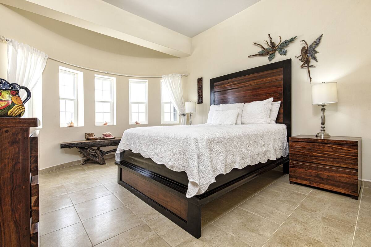 A bedroom with a large bed, a wooden nightstand, a bench, and a decorative wall piece.