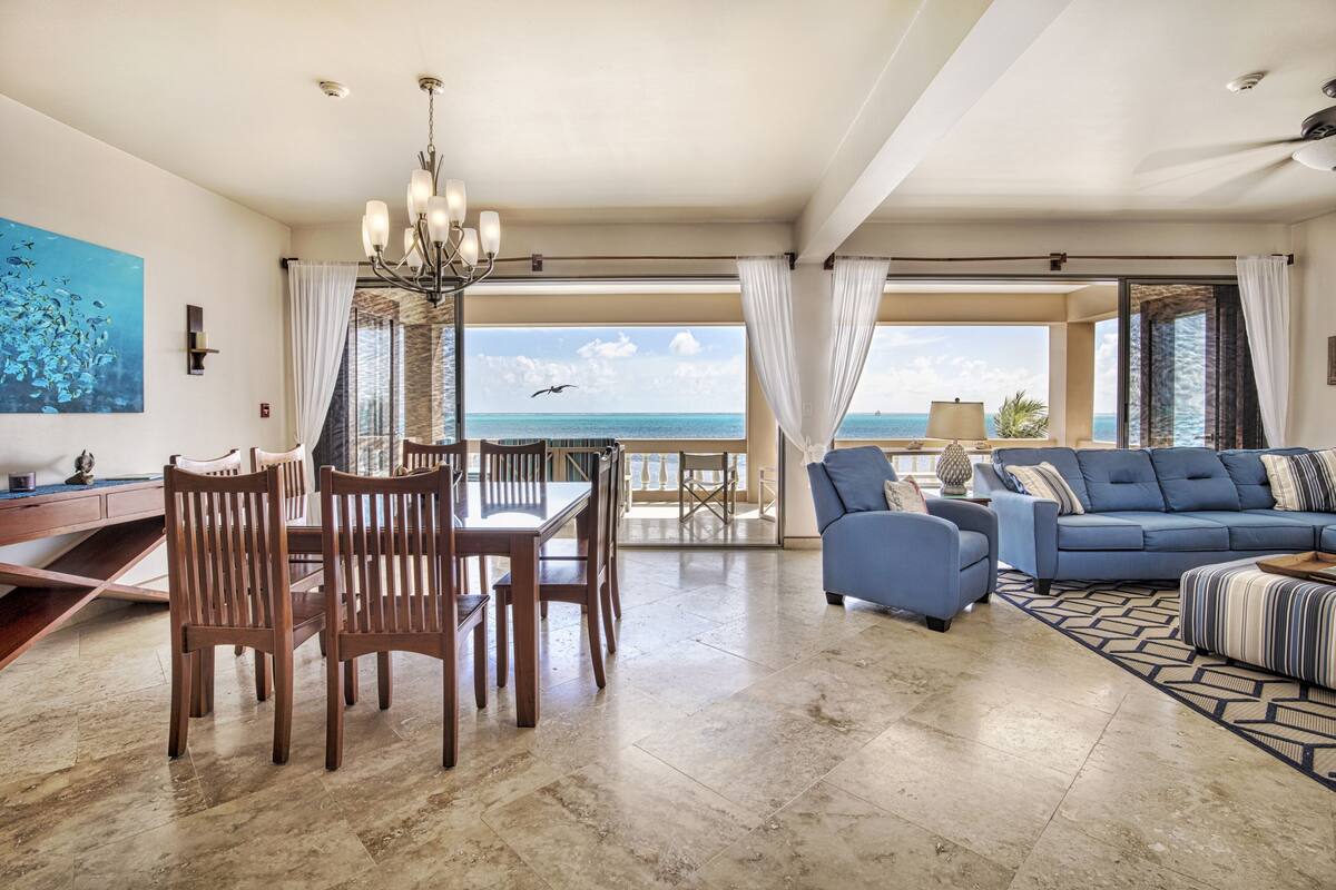 A spacious living area with a dining table and chairs, a blue sofa, and a view of the ocean.