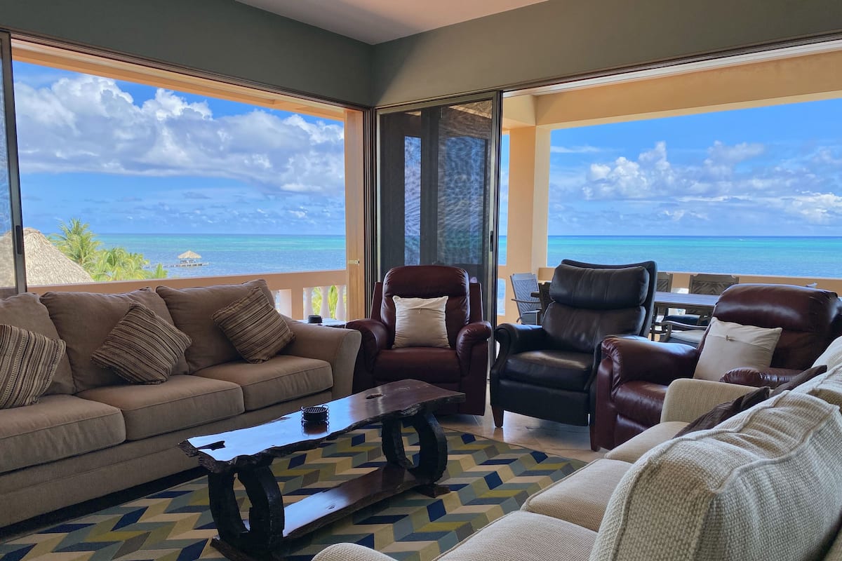 A living room with a sofa, two leather chairs, a coffee table, and a view of the ocean.