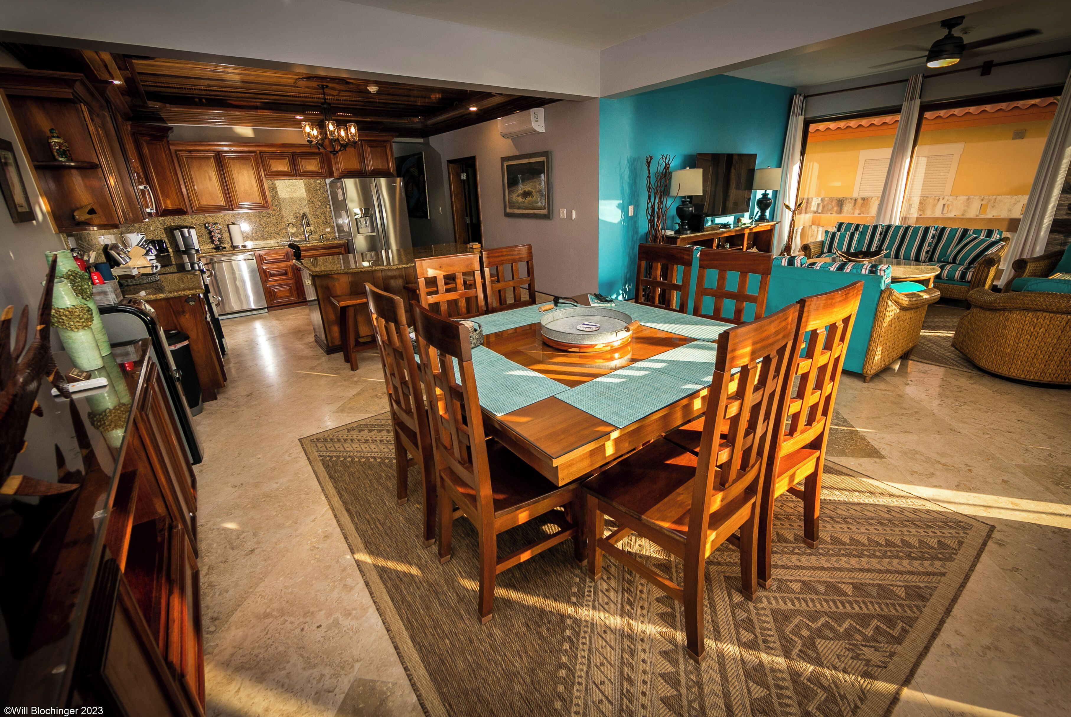Un comedor amplio con una mesa y sillas de madera, una cocina al fondo y una sala de estar con un sofá y televisor.