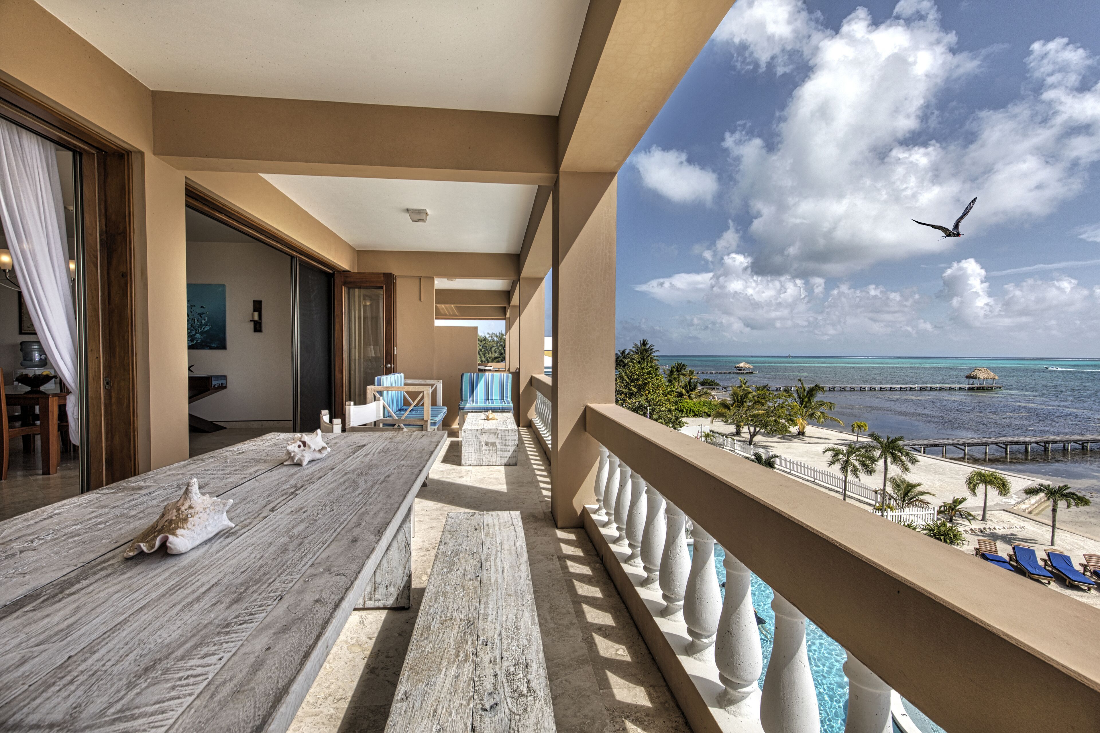 A balcony with a view of the ocean, a pool, and a pier.