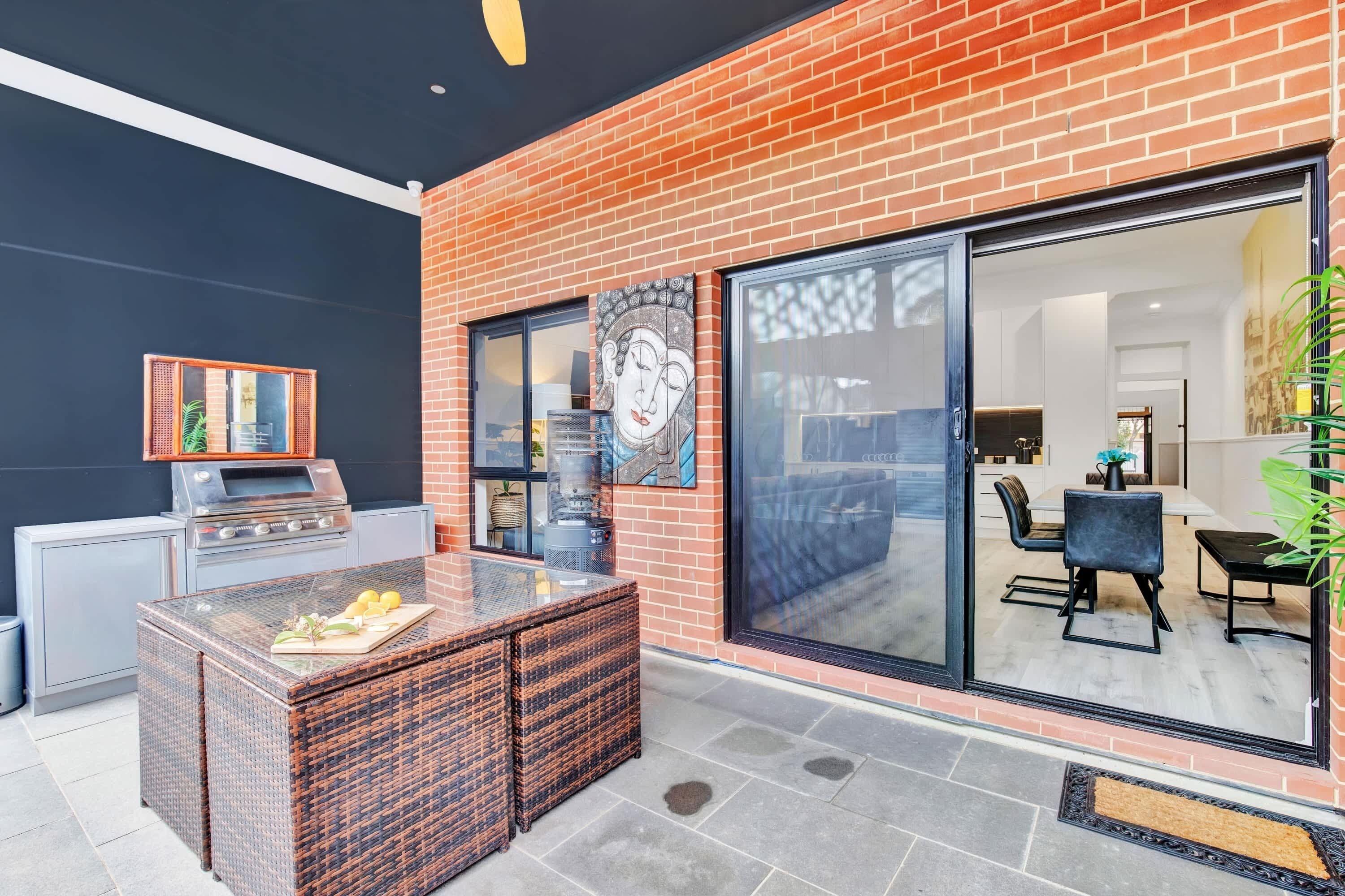 An outdoor patio with a grill, wicker furniture, and a glass door leading to an indoor dining area.