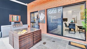 An outdoor patio with a grill, wicker furniture, and a glass door leading to an indoor dining area. - Noir Cottage | Glenelg North | 3BR | Netflix| BBQ (Glenelg North)