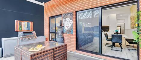 An outdoor patio with a grill, wicker furniture, and a glass door leading to an indoor dining area.