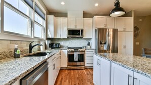 Una cocina moderna con armarios blancos, electrodomésticos de acero inoxidable, encimeras de granito y piso de madera.
