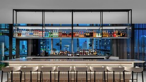 A modern bar with multiple shelves of liquor bottles, a long counter, and several bar stools. - Element by Marriott Miami Brickell (Miami)