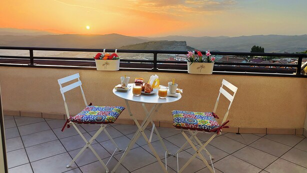 A dining table with chairs on a balcony with a sunset view.