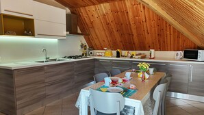 A modern kitchen with a wooden ceiling, white cabinets, and a dining area with a table set for four.