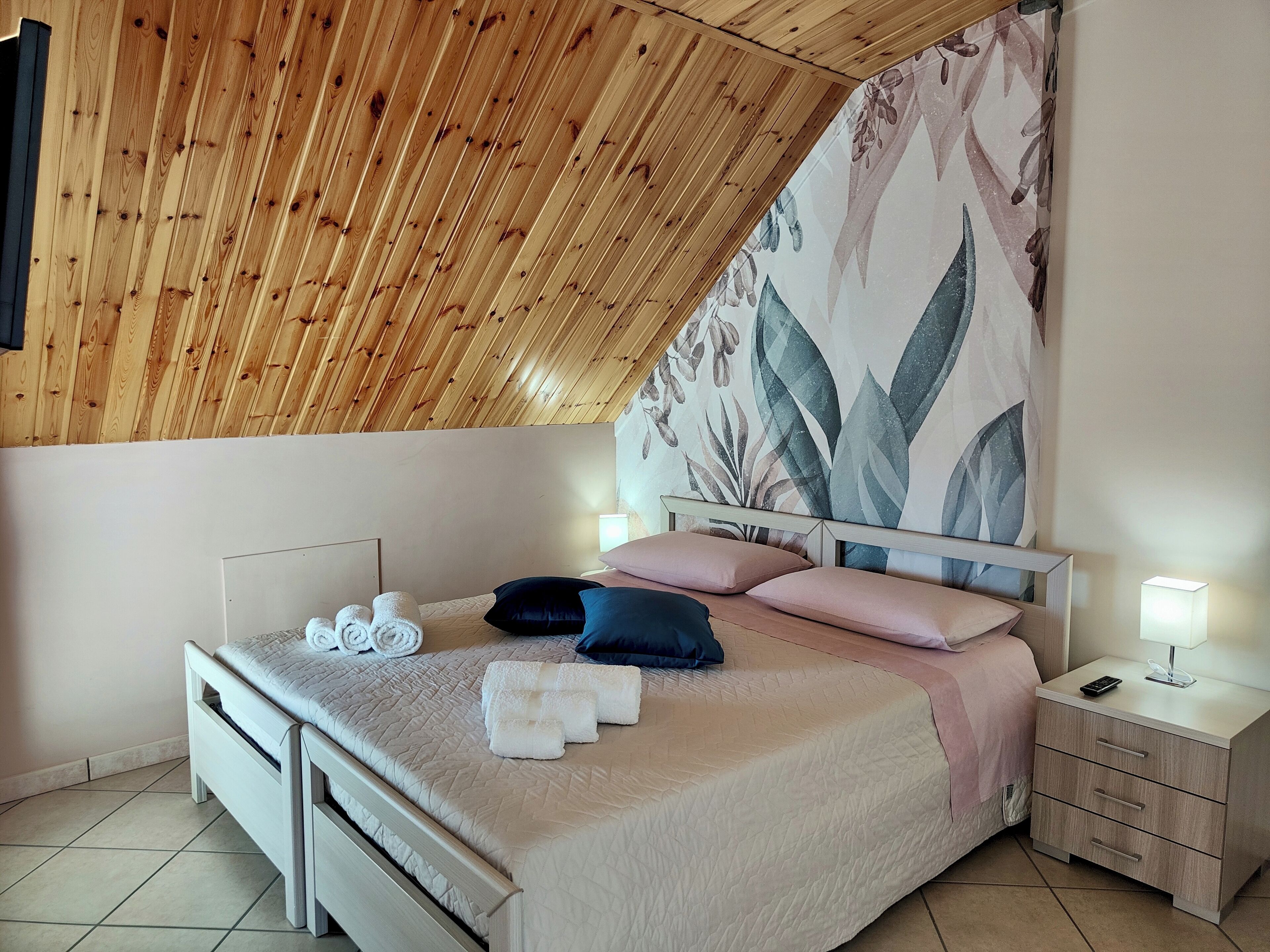 Un dormitorio con techo inclinado, una cama con cabecera, una mesita de noche y una pared con estampado floral.