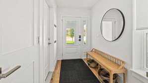 Un pasillo con puertas blancas, un banco, un espejo y una ventana.