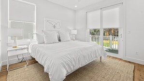 Un dormitorio con una cama grande, mesitas de noche blancas, un ventilador de techo y vistas a un balcón con paisaje exterior.