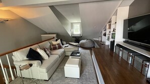 A modern loft-style living room with a white sofa, a coffee table, and a large flat-screen TV. - All-stop.  Rental Midships. (Annapolis)