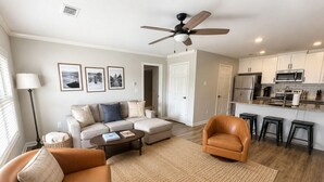 A living room with a sofa, armchair, coffee table, and a dining area with a kitchen in the background. - Walk to Toomer's! Ground-Floor 4 BR Auburn Condo (Auburn)
