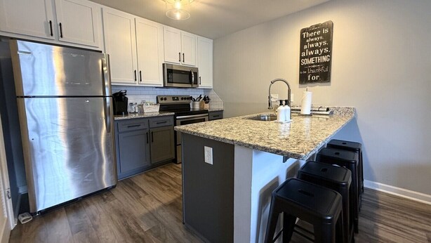 A modern kitchen with stainless steel appliances, a granite countertop, and a bar stool area. - Walk to Toomer's! Ground-Floor 4 BR Auburn Condo (Auburn)