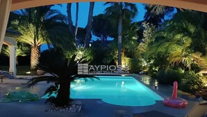 A luxury villa with a swimming pool surrounded by palm trees and a well-lit outdoor area.
