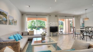 A spacious living room with a sofa, coffee table, and a TV. There are large windows and a view of the outdoors.