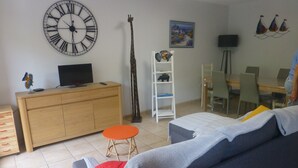 A living room with a large wall clock, a sofa, a dining table, and a TV. - Pleasant apartment 2 steps from downtown  (Port-Vendres)