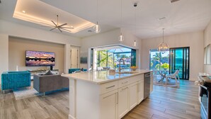 Une cuisine moderne dotée d’un îlot central, de meubles blancs et d’une grande fenêtre offrant une vue sur l’extérieur.