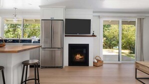 A modern kitchen with a built-in fireplace, a large TV, and a sliding glass door leading to a garden. - Perch - Greenbank Cottage: quiet & view, relaxing outdoor oasis (Greenbank)