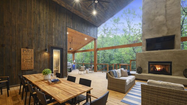 A wooden deck with a dining table and chairs, a fireplace, and a sofa. - New on Creek! HUGE Deck - Luxury Sleeps 15 - 4 Bedrooms (Broken Bow)