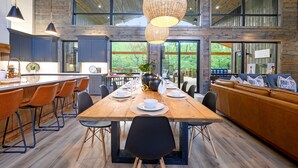A spacious dining area with a wooden table, black chairs, and a leather sofa. - New on Creek! HUGE Deck - Luxury Sleeps 15 - 4 Bedrooms (Broken Bow)