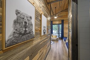 A hallway with wooden walls and ceiling, featuring large bear paintings, a sofa with cushions, and a view of the outdoors.