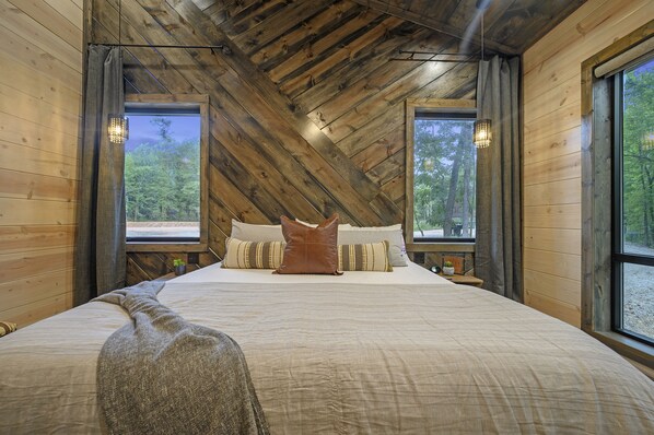 Une chambre avec un grand lit, des murs en bois et une vue sur l’extérieur.