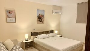 A bedroom with a bed, bedside tables, a lamp, a sofa, and two wall-mounted air conditioners.