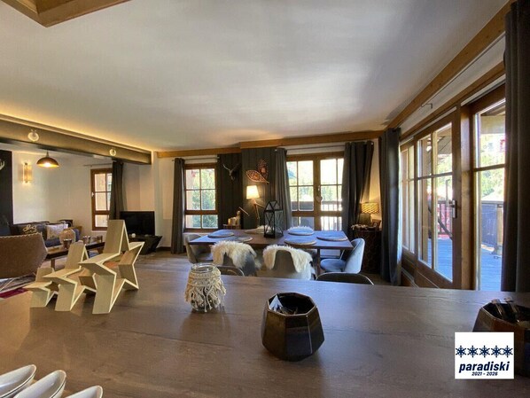 Un vaste espace de vie doté d’une grande table en bois, de nombreux sièges et de grandes fenêtres laissant entrer la lumière naturelle.