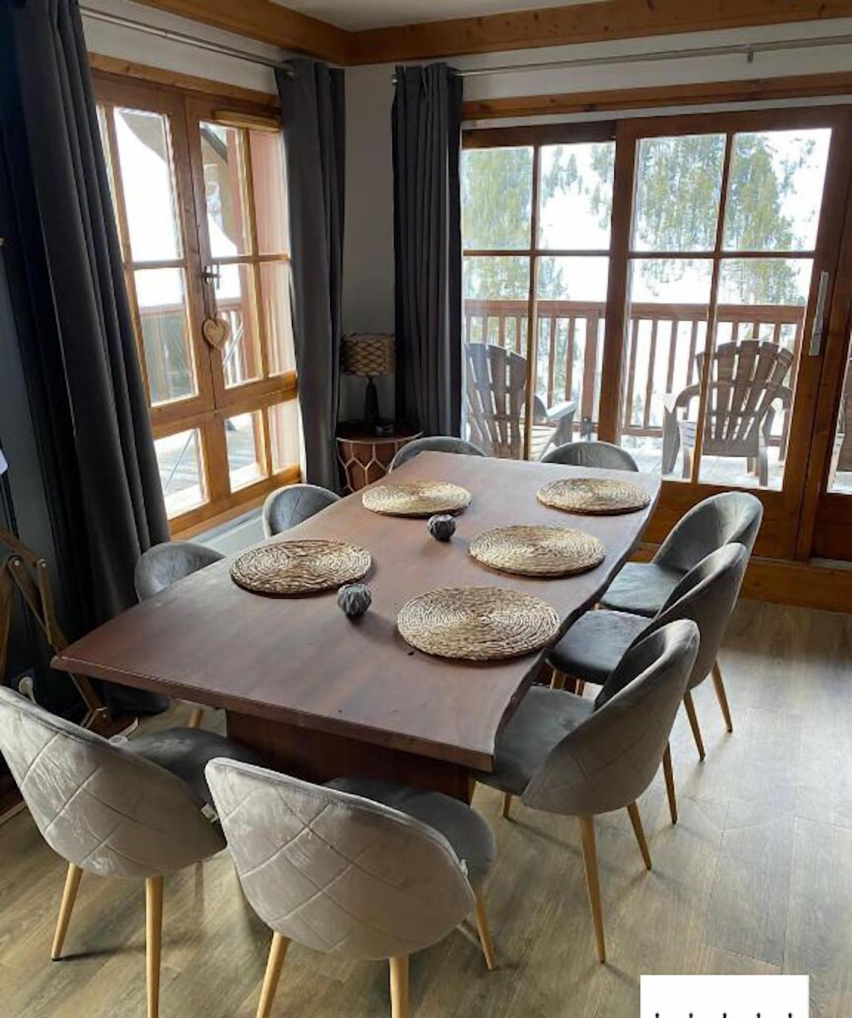 Un espace repas avec une longue table en bois, des chaises à revêtement gris et des sets de table en fibres tressées.