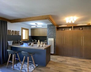 A modern kitchen with a central island, bar stools, wooden cabinets, and a stone accent wall.