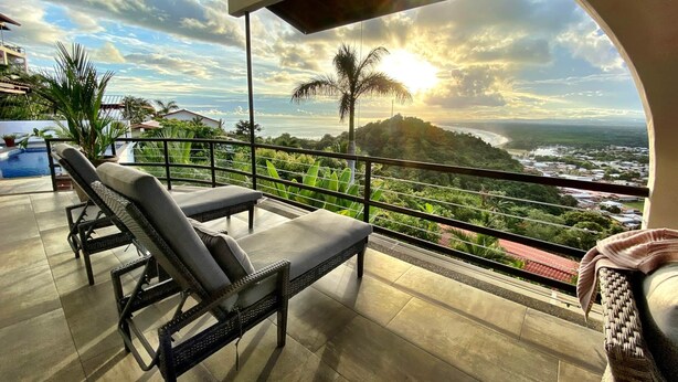Een balkon met rieten lounge fauteuils, een zwembad en uitzicht op zee en een stad.