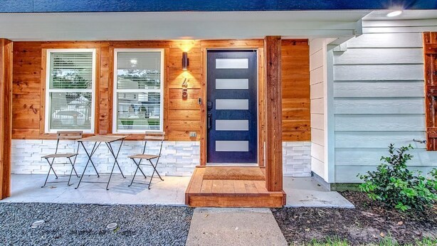 Ett modernt hus med en träfasad, en mörk ytterdörr och en liten veranda med ett bord och några stolar.