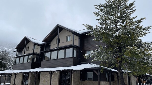 A multi-story building with a stone facade and large windows, surrounded by snow-covered ground and trees.