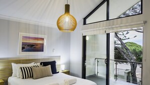 Un dormitorio con una cama grande, una lámpara colgante, un cuadro enmarcado en la pared y una puerta corrediza de vidrio que da a un espacio exterior.