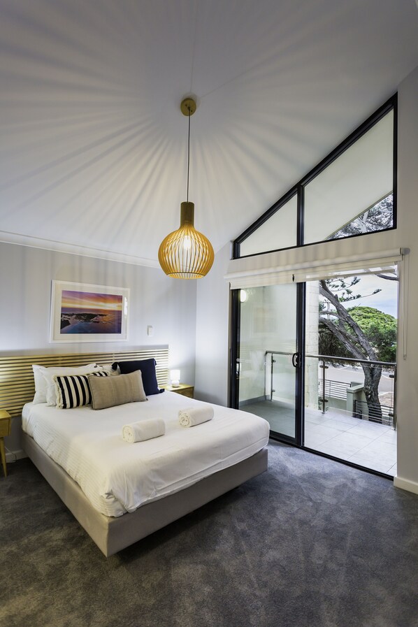 A bedroom with a large bed, a hanging light fixture, a framed picture on the wall, and a sliding glass door leading to an outdoor area.