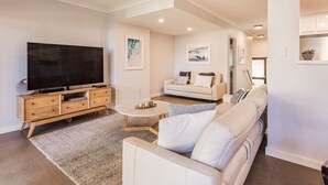 Una sala de estar moderna con televisor de pantalla plana, mueble bajo de madera, sofá color beige y una mesita de centro.