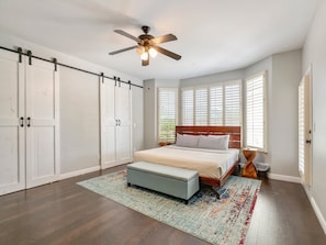 A bedroom with a bed, a ceiling fan, a window with blinds, a wardrobe, and a rug.