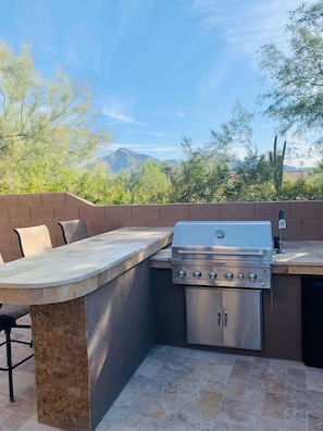 Una cocina al aire libre con una parrilla, asientos y piso de baldosas de piedra.