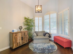 A living room with a wooden cabinet, a large potted plant, a grey sofa, a red bench, and a patterned rug.