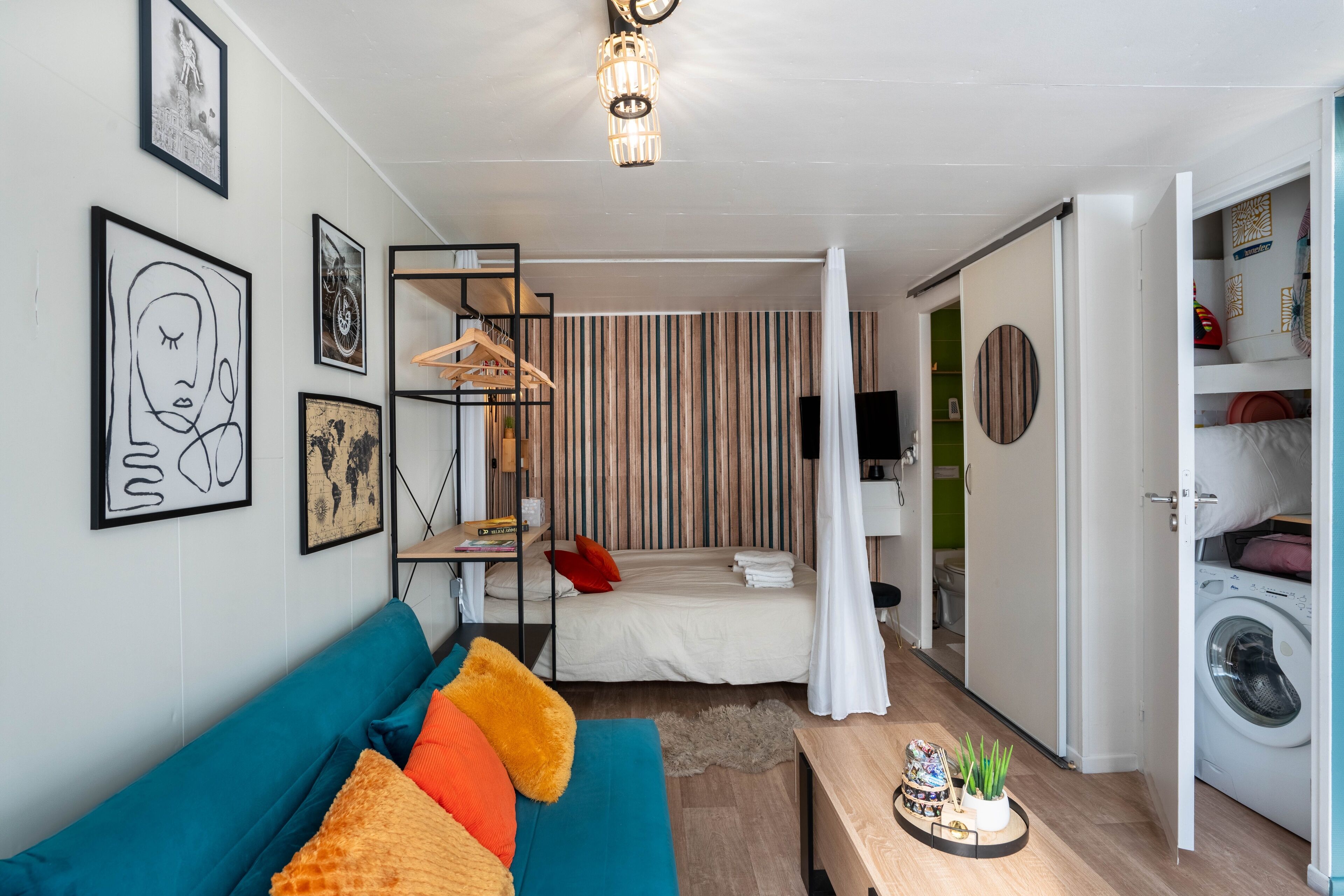 Une pièce compacte et moderne, comprenant un canapé, un lit, une petite table et un lave-linge.