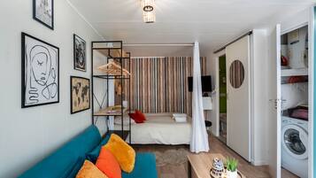 Une pièce compacte et moderne, comprenant un canapé, un lit, une petite table et un lave-linge.