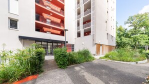 Un bâtiment moderne avec une entrée centrale, entouré de verdure et d’une zone pavée.
