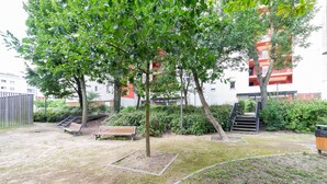Une cour avec un banc, des arbres et un bâtiment aux balcons rouges en arrière-plan.