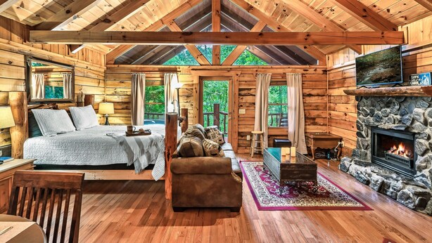 A log cabin interior with a bed, sofa, fireplace, and a television. - Quiet Cabin in Woods- Alpine Ridge Sub-Division - 1 Bed/1Bath Jaccuzi (Sevierville)