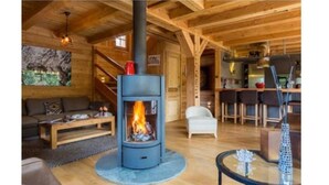 Interior acogedor de una cabaña con estufa de leña en el centro, comedor y sala de estar con sofá y mesa de centro.